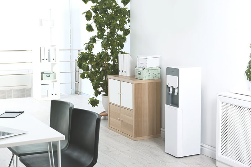 Büro mit weißen Wasserspender, Holzkommode und Pflanze