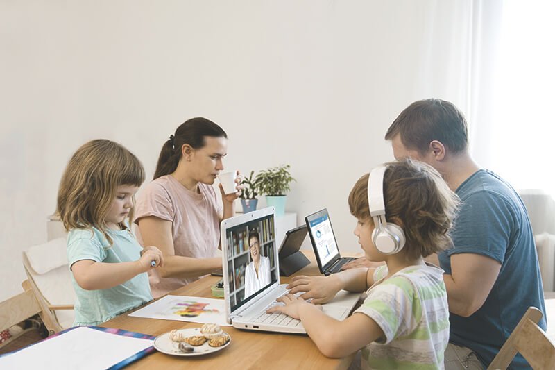 Eltern sitzen am Tisch mit Kindern und Laptops
